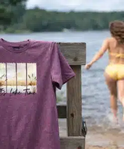 Woman running into the lake with “It’s Lake Time” t-shirt hanging on dock railing in summer sunshine