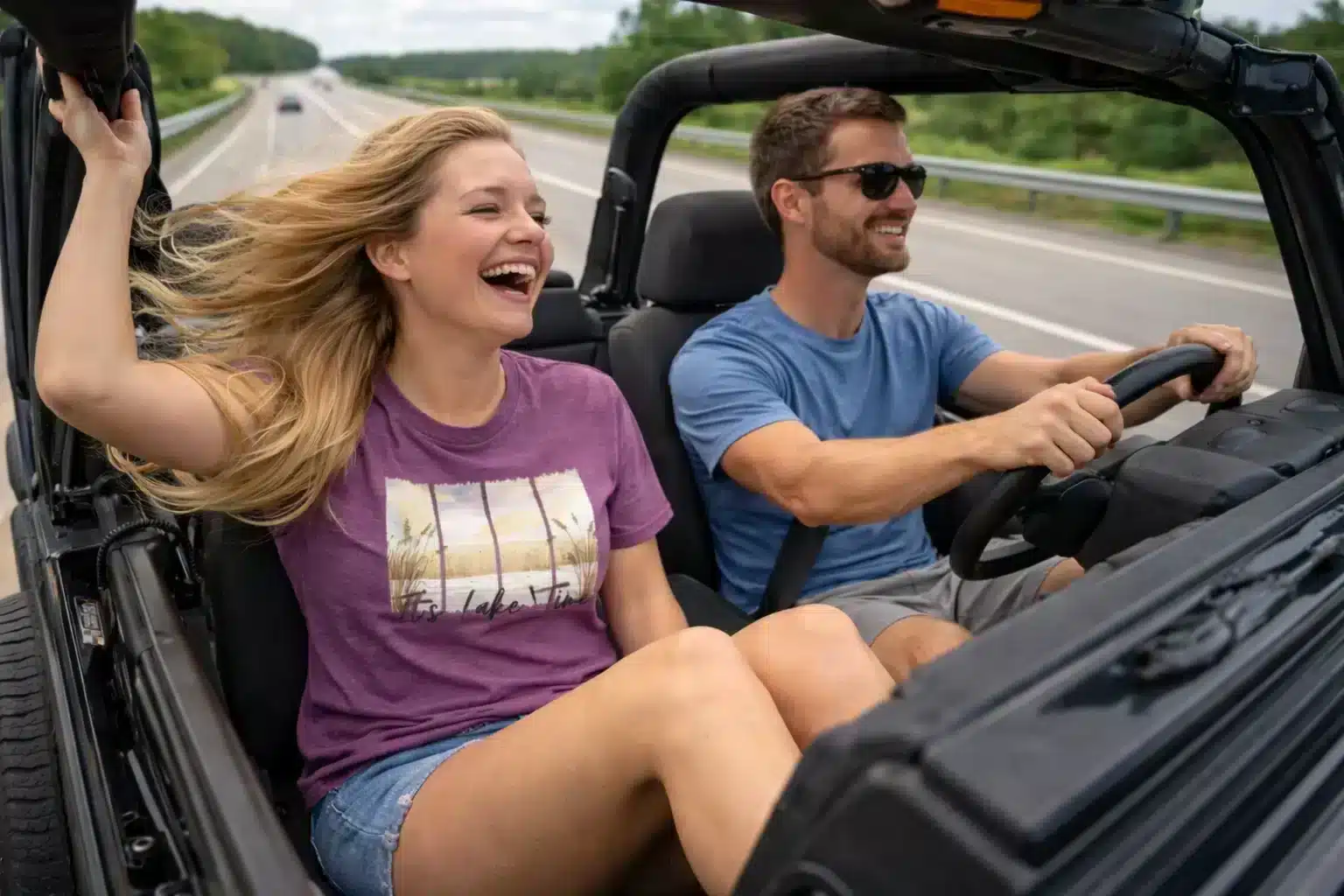 Couple driving doorless Jeep wearing “It’s Lake Time” t-shirts on a summer highway adventure
