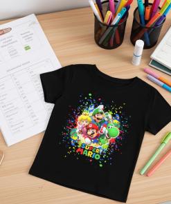 This girls black tee is packed with bold colors and playful energy, it features four of the most iconic characters from the Nintendo universe. It is laying on a desk sounded by school items.
