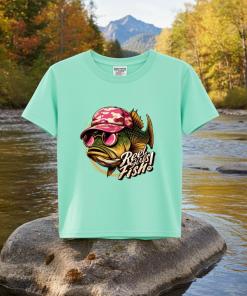 This t-shirt features a bold bass fish wearing red lenses sunglasses and a brown-and-red baseball cap. The fun caption “Reel Girls Fish!” It is standing over a rock.
