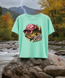 This t-shirt features a bold bass fish wearing red lenses sunglasses and a brown-and-red baseball cap. The fun caption “Reel Girls Fish!” The sky is cloudy and lighting is visible in the background.
